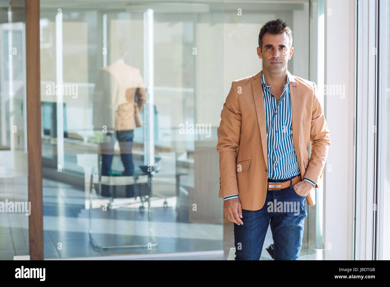 A 35 40 ans caucasien homme cheveux noirs cool look moderne avec la main dans la poche dans une chemise jeans et blazer dans un bureau medium long shot Photo Stock Alamy