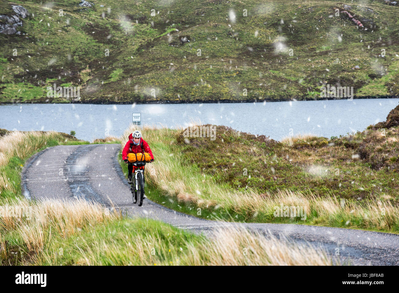 Lonely biker vélo dans les Highlands écossais, lourdement chargé sur vélos de cyclotourisme le long de la route à voie unique au cours de la neige au printemps, Ecosse, Royaume-Uni Banque D'Images
