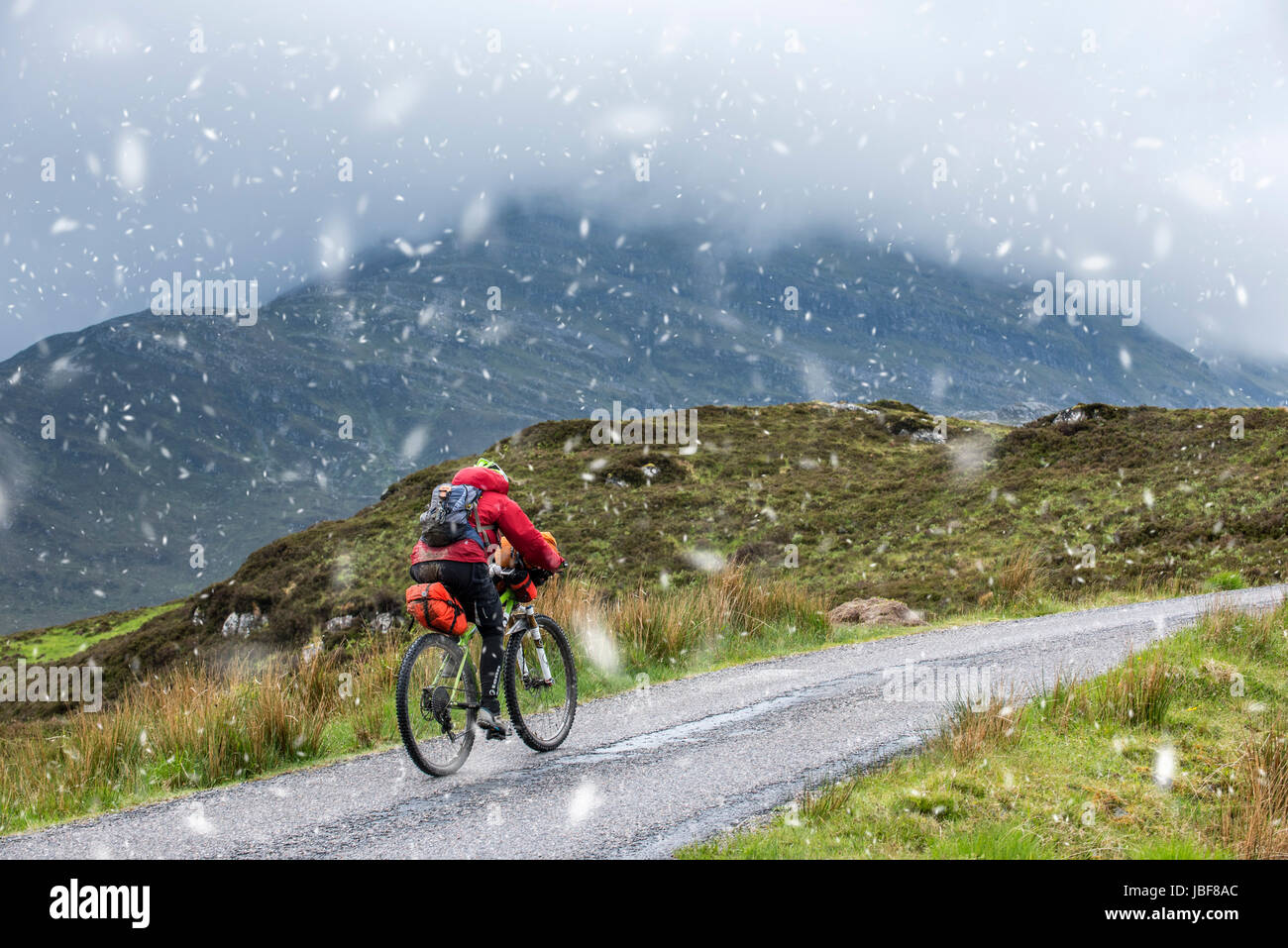 Lonely biker vélo dans les Highlands écossais, lourdement chargé sur vélos de cyclotourisme le long de la route à voie unique au cours de la neige au printemps, Ecosse, Royaume-Uni Banque D'Images