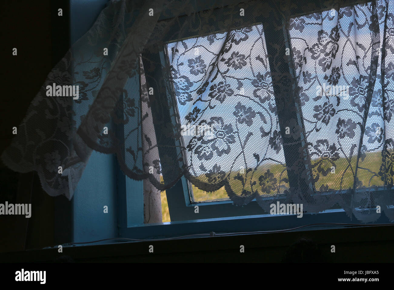 Rideau de dentelle à l'ancienne un souffle une brise marine qui est venu à travers une fenêtre légèrement ouverte ; ciel bleu et vert de l'herbe à l'extérieur un jour de printemps. Banque D'Images