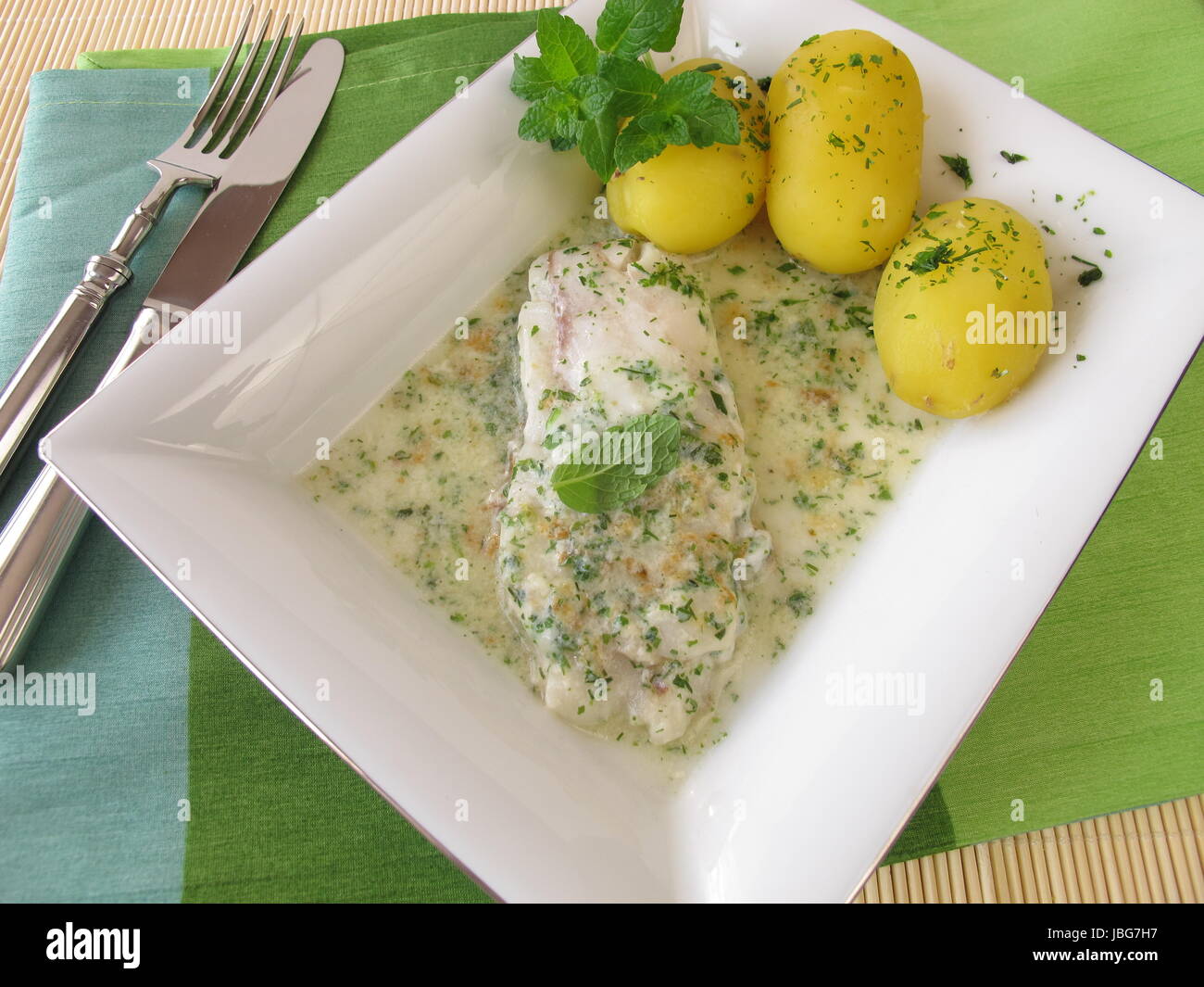 Le poisson sur les pommes de terre avec sauce aux fines herbes Banque D'Images