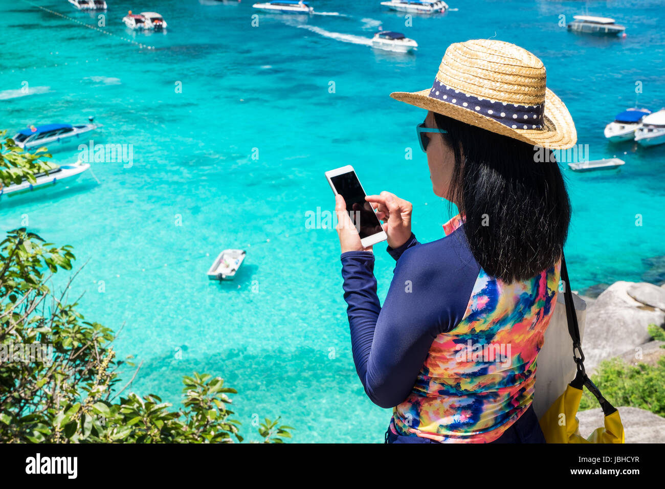 Traveller femme avec maillot coloré utiliser mobile prendre une photo de vue en haut de la montagne et de la mer en bateau de vitesse,les vacances d'été en voyage. Banque D'Images