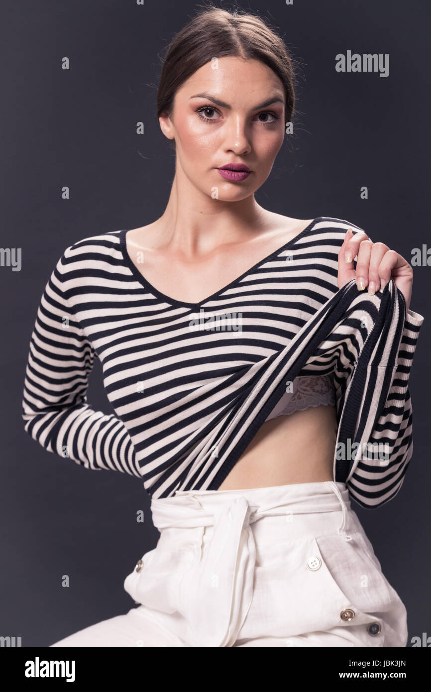 Une jeune femme de race blanche 20s, 29 ans, mannequin, poser, studio, fond blanc, horizontal stripe shirt, pantalon blanc, à la recherche d'appareil photo Banque D'Images