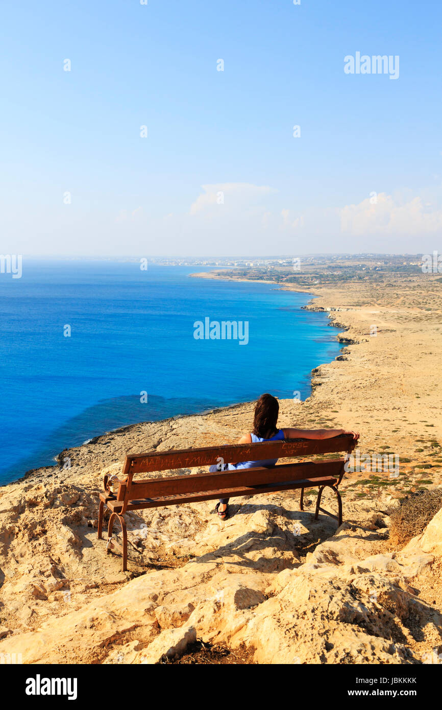Une seule femme assise sur un banc à Cape Greco falaise donnant sur la mer Méditerranée vers Ayia Napa au loin. Chypre. Banque D'Images
