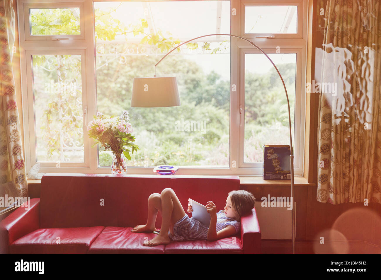 Boy reading, using digital tablet sur salon canapé Banque D'Images