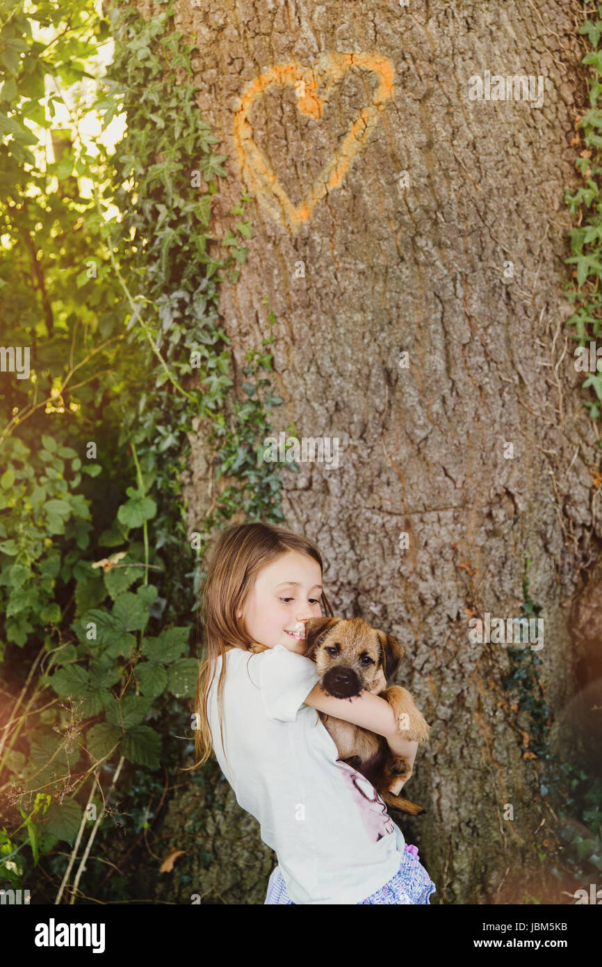 Girl holding puppy dog ci-dessous avec l'arbre en forme de coeur Banque D'Images