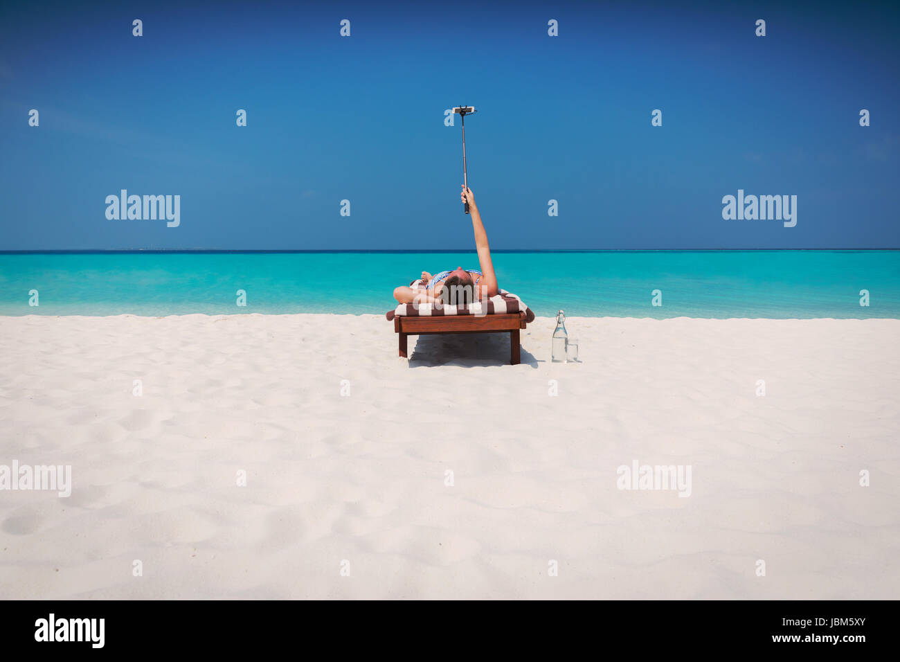 Woman, bronzer et prendre des selfies selfies avec stick on lounge chair on sunny beach Banque D'Images