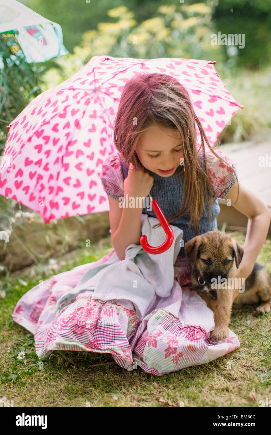 Fille avec puppy dog holding heart-shape parapluie dans l'herbe Banque D'Images