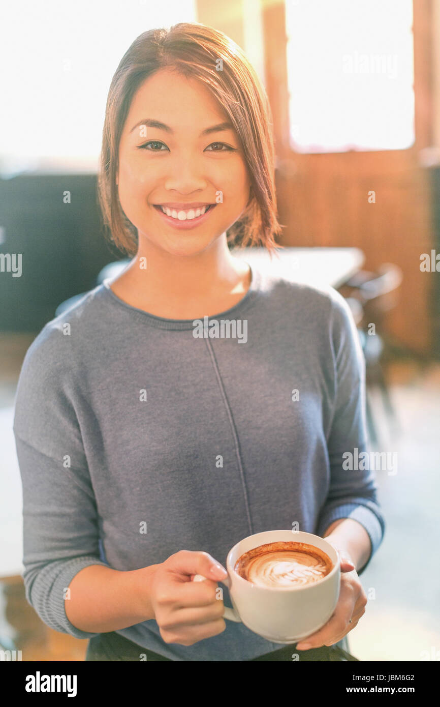 Portrait of smiling Chinese woman drinking cappuccino au café Banque D'Images