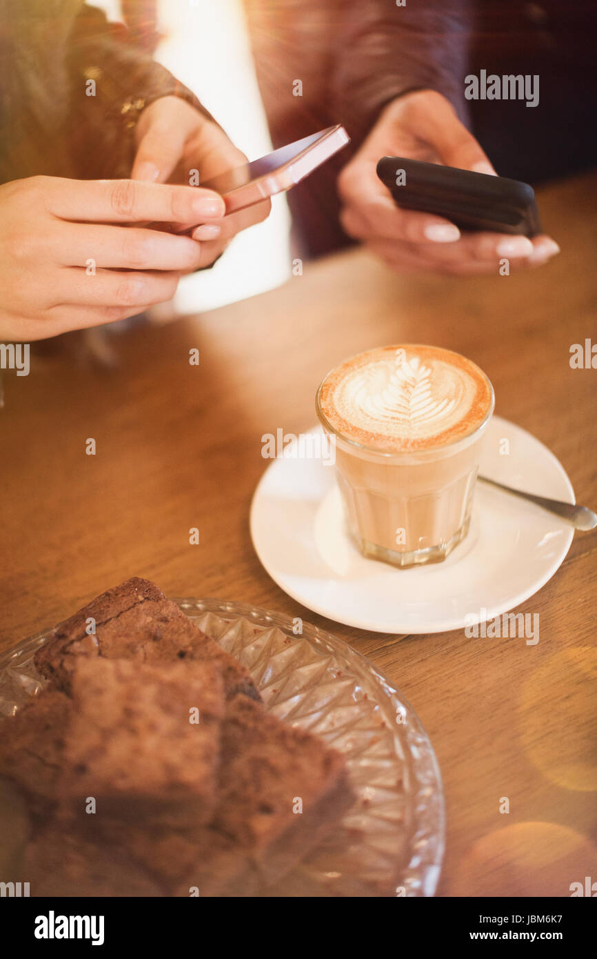 Les femmes avec les téléphones avec appareil photo photographier un cappuccino au café tableau design Banque D'Images