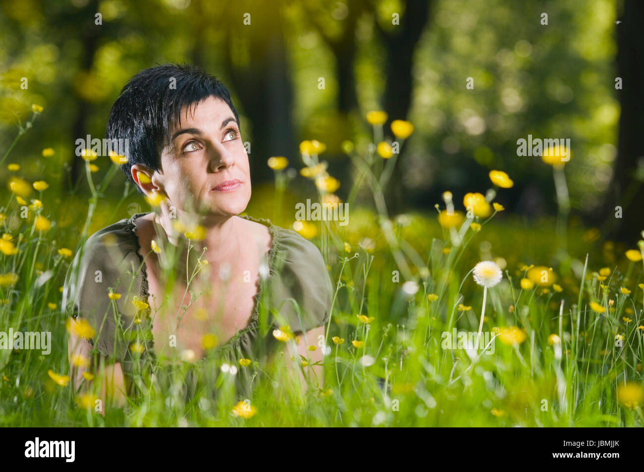 Frontale Kopf-und-Schulter-Ansicht schwarzhaarigen Frau und mittleren modifie auf dem Bauch im Gras mit gelben Blüten liegend verträumt nach rechts oben blickend Banque D'Images