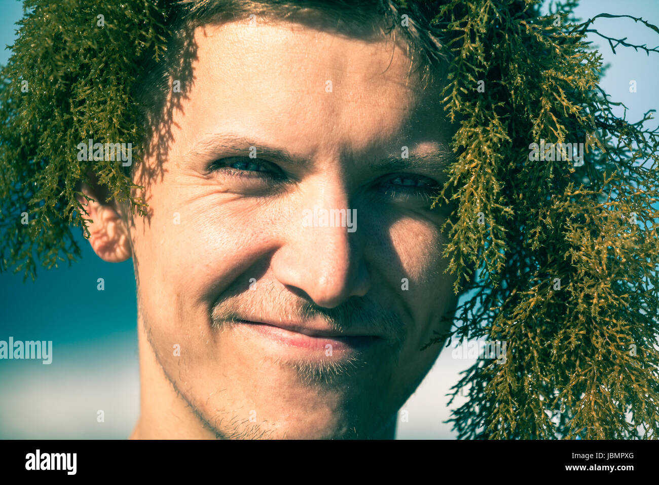 Gros plan du jeune homme souriant avec des algues sur la tête. Banque D'Images