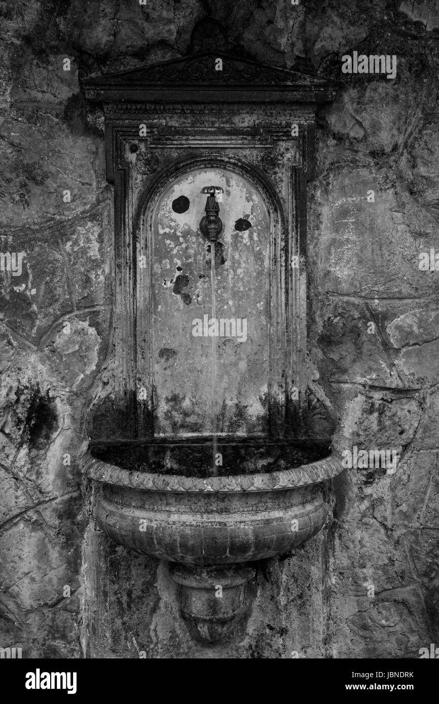 Fontaine italienne-, ancienne fontaine coulant italien. Belle coupe de main ornate stone contre une pierre et plâtre en toile de fond. Noir et blanc. L'Ombrie, Italie Banque D'Images