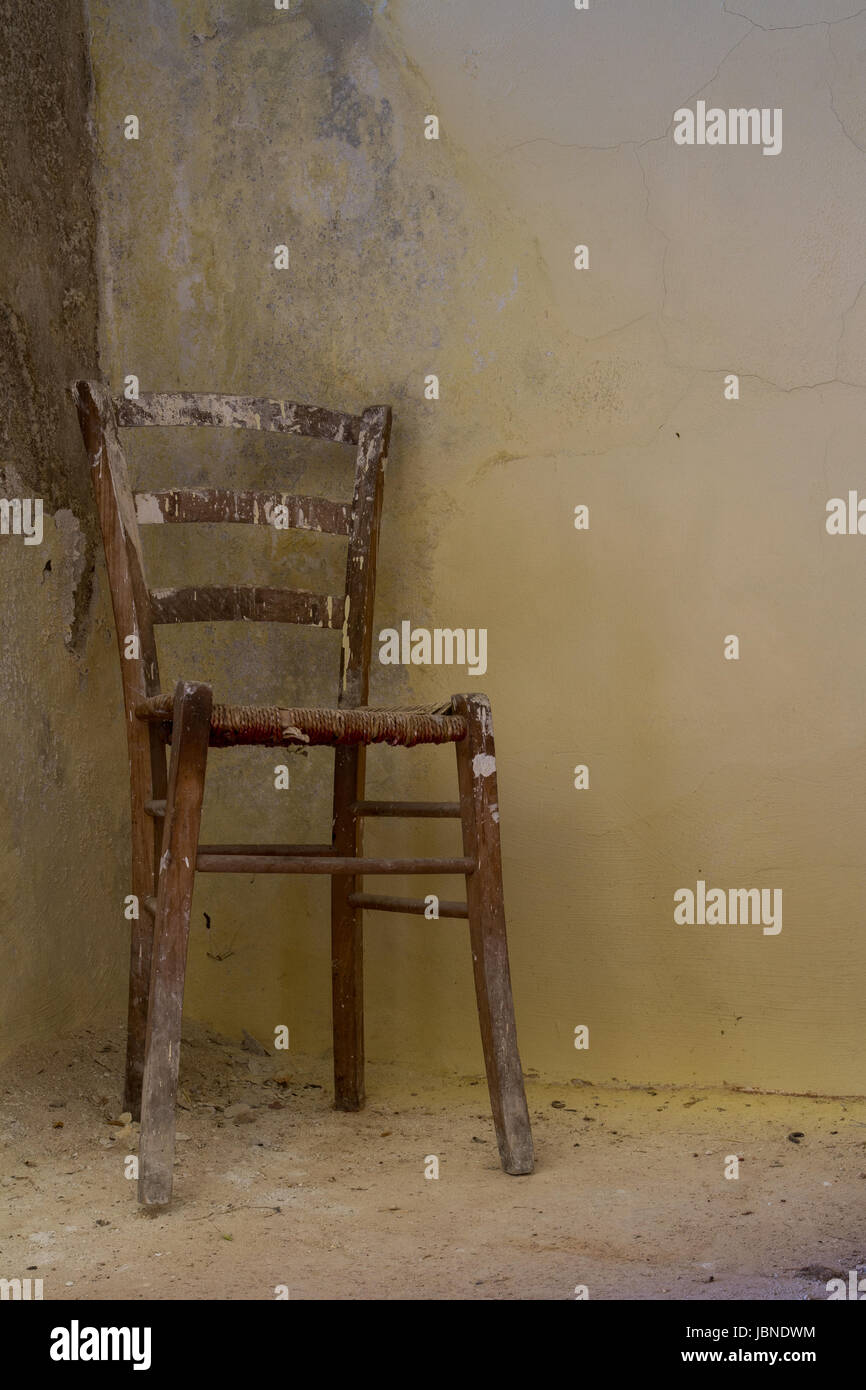 Prendre un Siège- une peinture primitive et météo éclaboussé le président est assis dans le coin d'une maison abandonnée contre un mur crépi jaune. Banque D'Images
