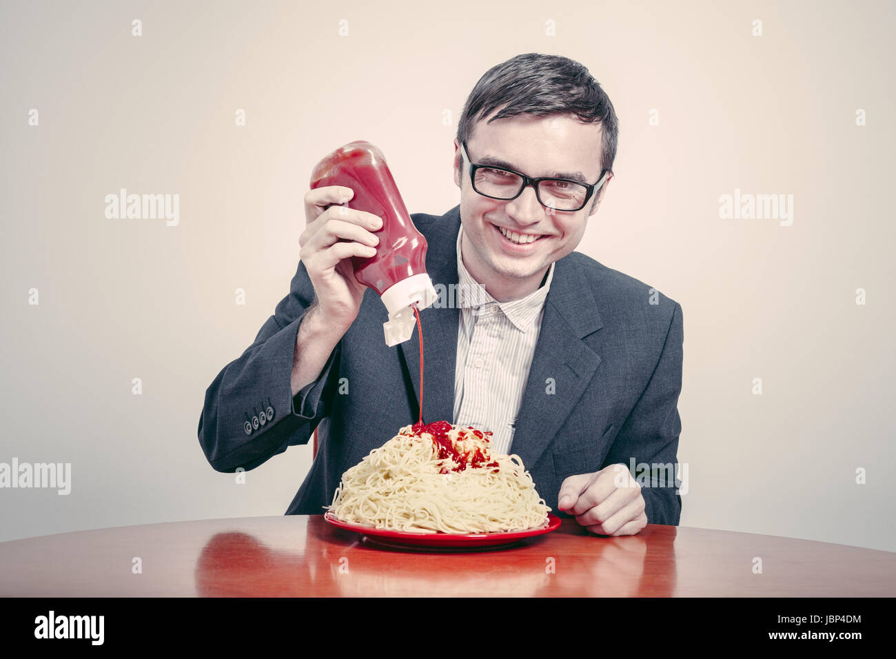 Le consumérisme positive concept. Happy businessman pouring ketchup sur grand plat de pâtes. Banque D'Images