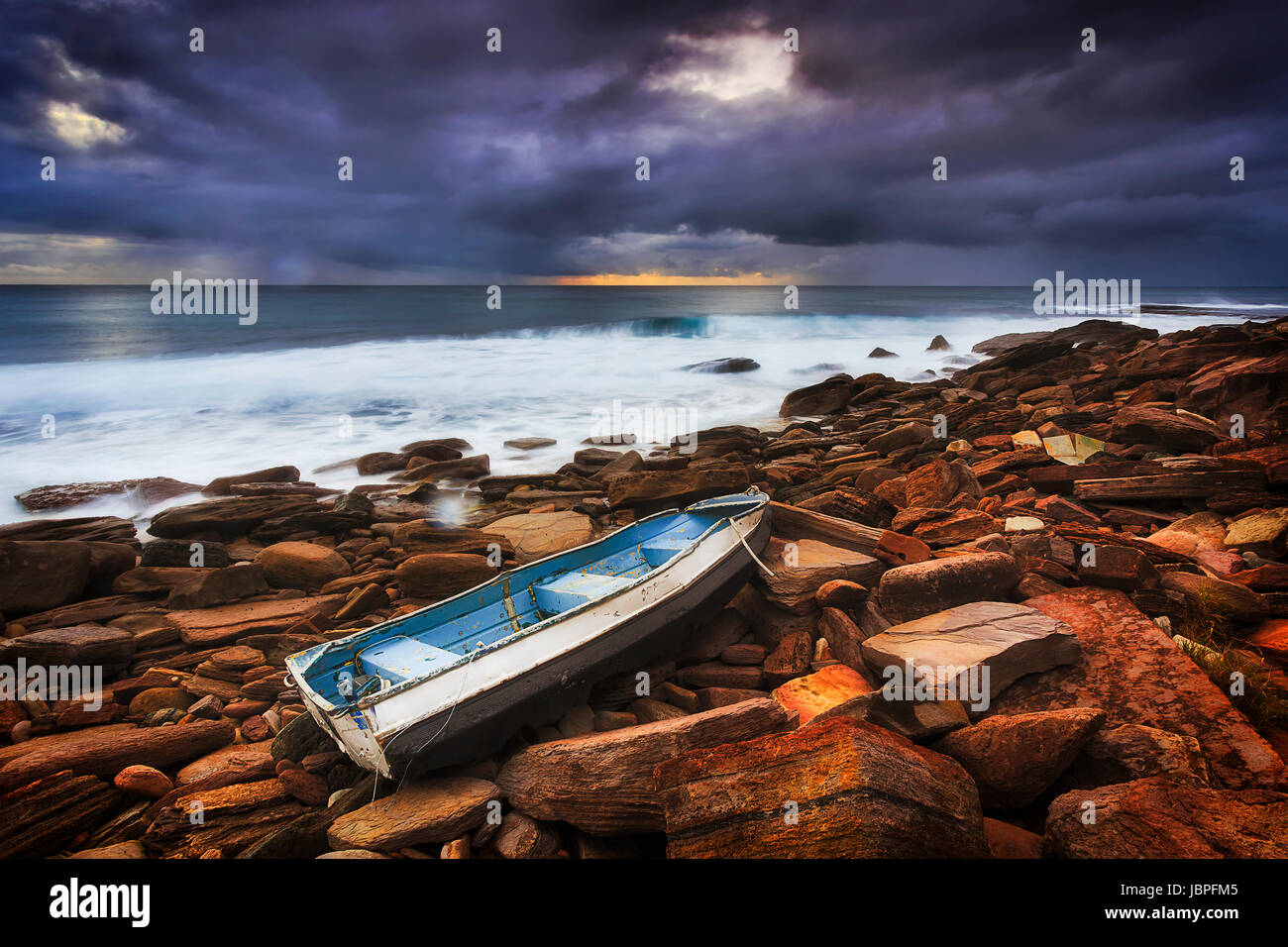 Des rochers et de roches érodées à Bungan beach plages du nord de Sydney durant une tempête lever du soleil avec lonely petit bateau de pêche à terre. Banque D'Images