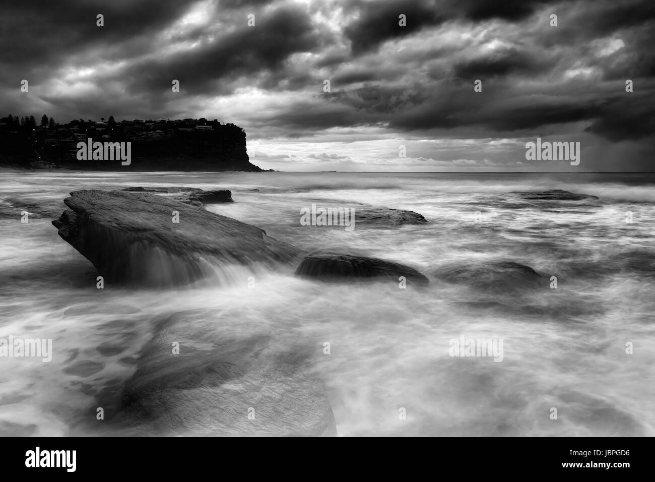 Conditions météorologiques orageuses spectaculaires au large de Sydney Pacific aroudn Bungan beach avec des rochers submergés survolés par des vagues en noir-blanc co Banque D'Images