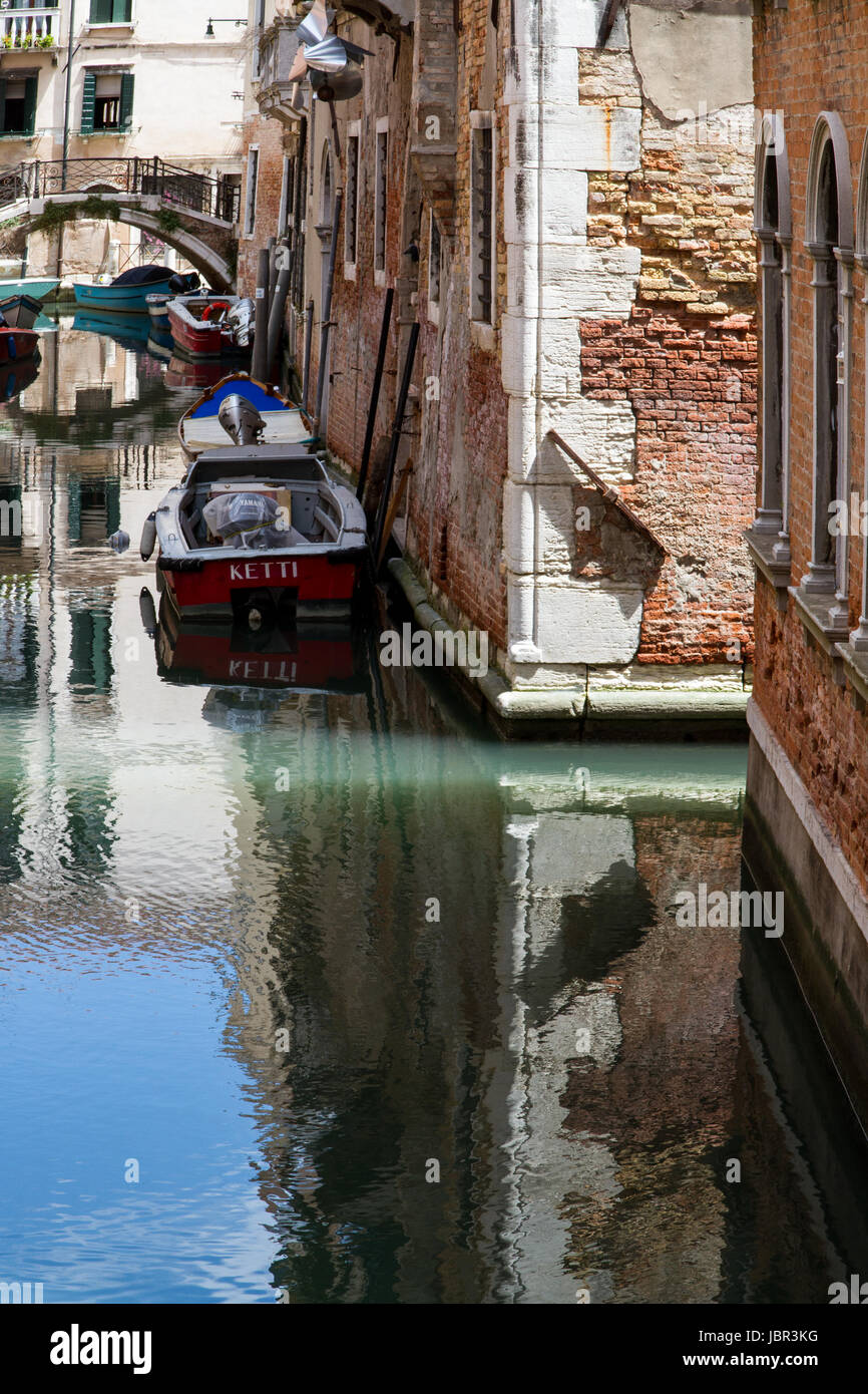 Canal de Venise- Un arbre de lumière transforme le turquoise de l'eau dans le canal, des bateaux et des bâtiments se reflètent sur sa surface à Venise, Italie Banque D'Images