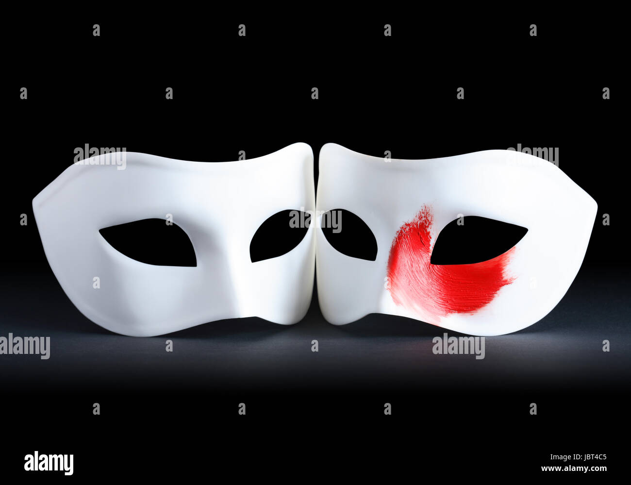 Deux masques blancs sur fond noir. Un masque avec touche de peinture rouge Banque D'Images