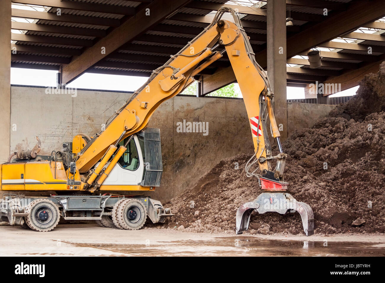 Bagger mit Greifarm vor einem großen Haufen brauner Erde dans der Bauindustrie Banque D'Images