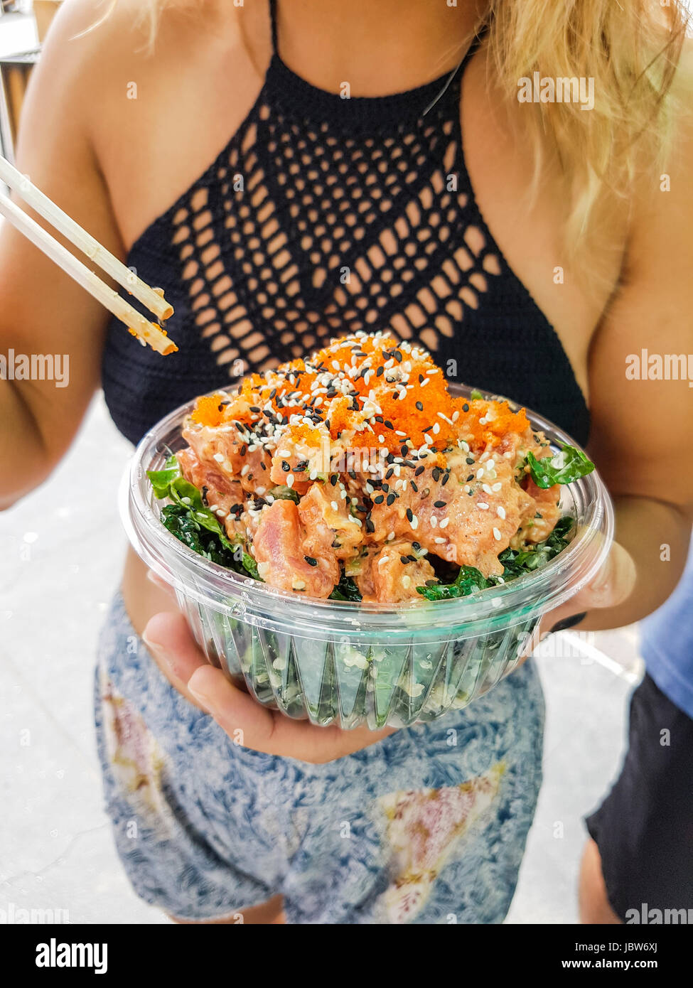 Mid section of young woman eating bowl poke à Hermosa Beach, Californie, USA Banque D'Images