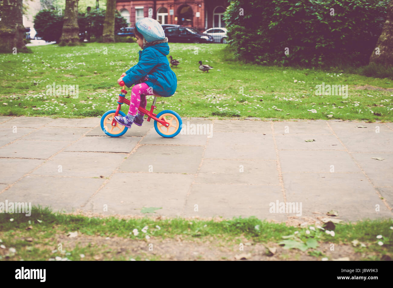 Jeune fille de quatre ans est de la suspendre le vélo dans le parc. Elle est d'apprendre à faire du vélo et elle porte un casque de sécurité. Banque D'Images