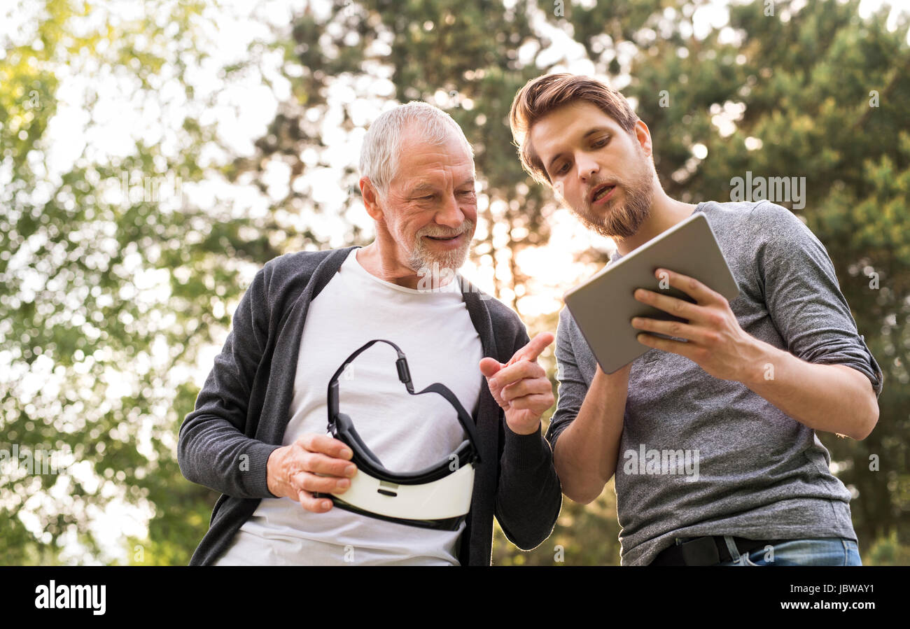 Jeune homme et son père senior avec lunettes VR à l'extérieur. Banque D'Images