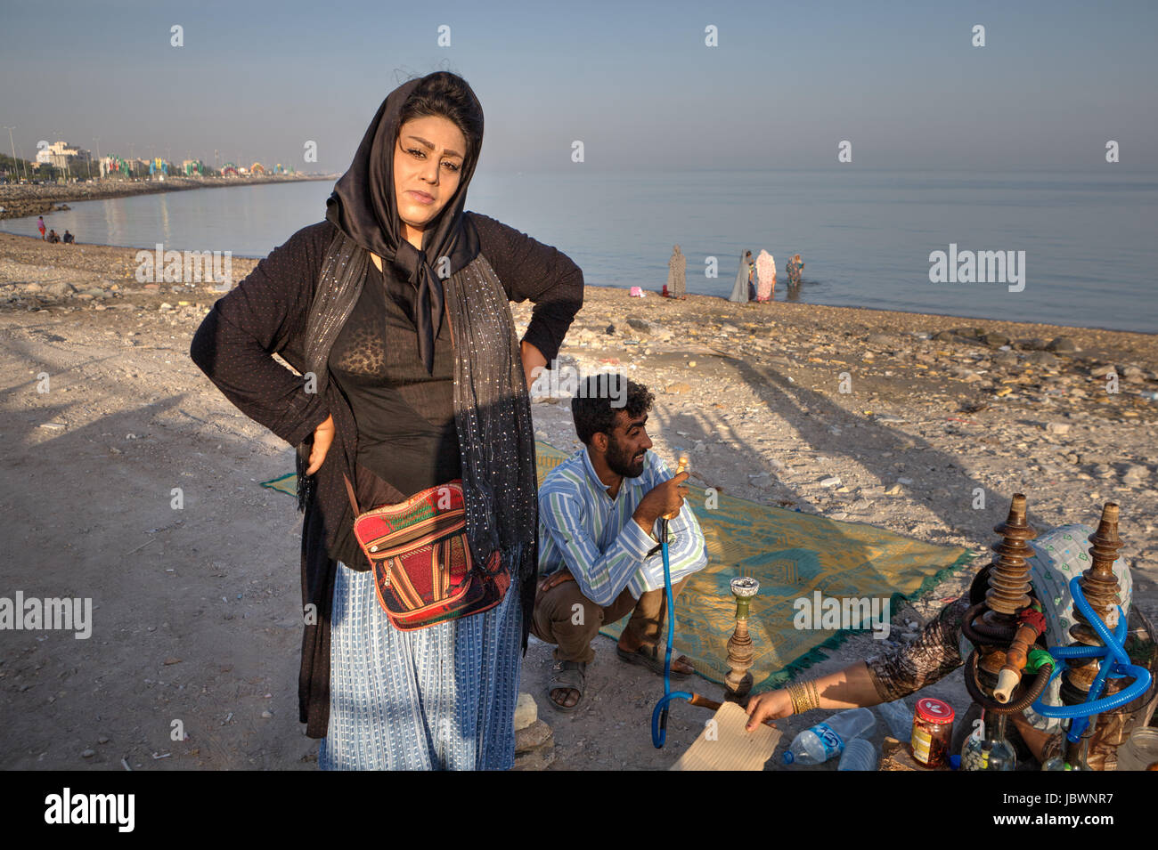 Bandar Abbas, Iran, Province Hormozgan - 16 avril, 2017 : Une femme portant un hijab iranien se tient près d'un fumeur de narguilé sur un beau soir, sur la rive Banque D'Images