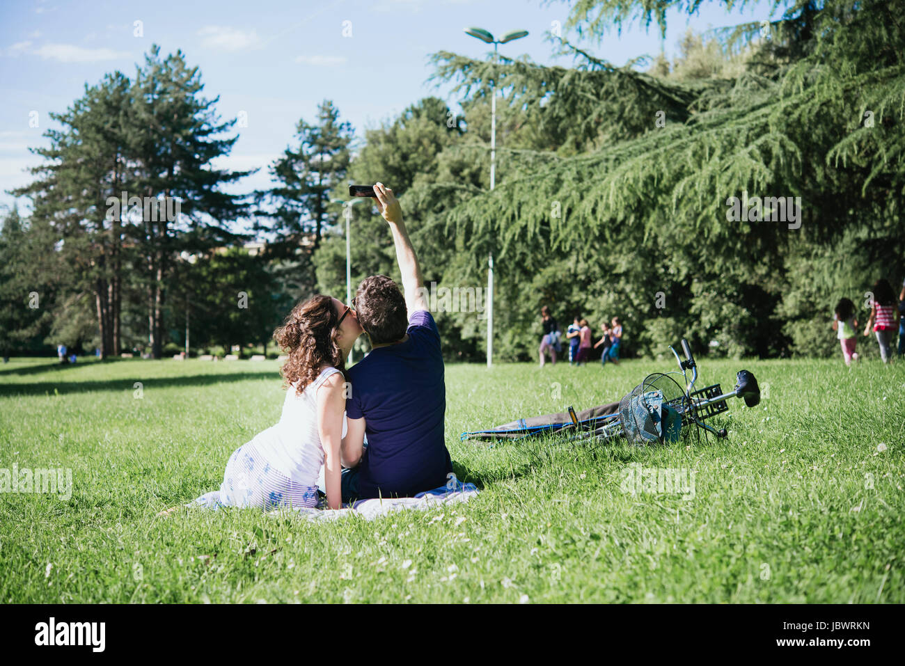 Vue arrière du couple qui tout en restant assis dans selfies smartphone park, Arezzo, Toscane, Italie Banque D'Images