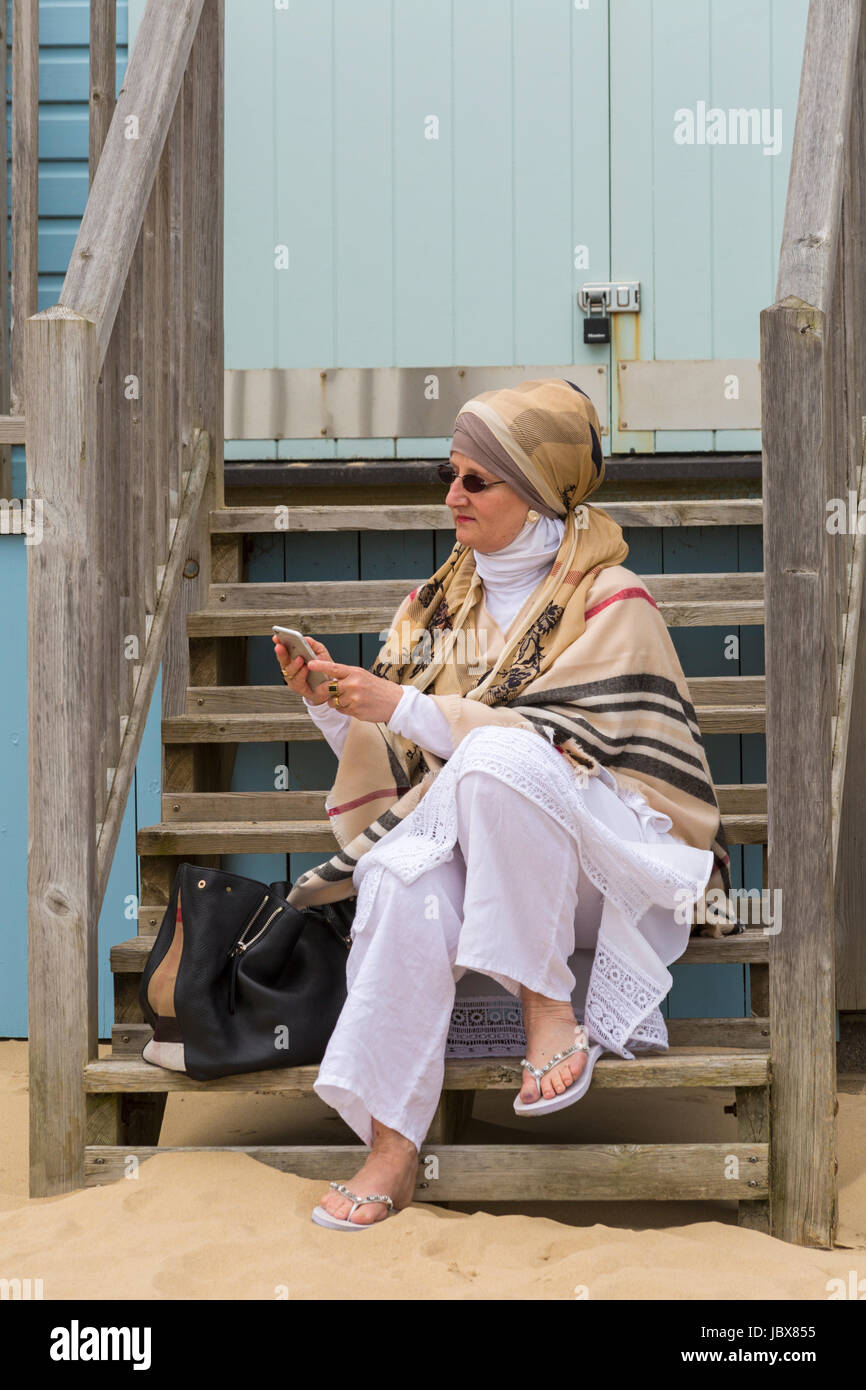 Woman looking at iphone téléphone mobile alors qu'il était assis sur les marches de beach hut à Bournemouth, Alum Chine en juin Banque D'Images