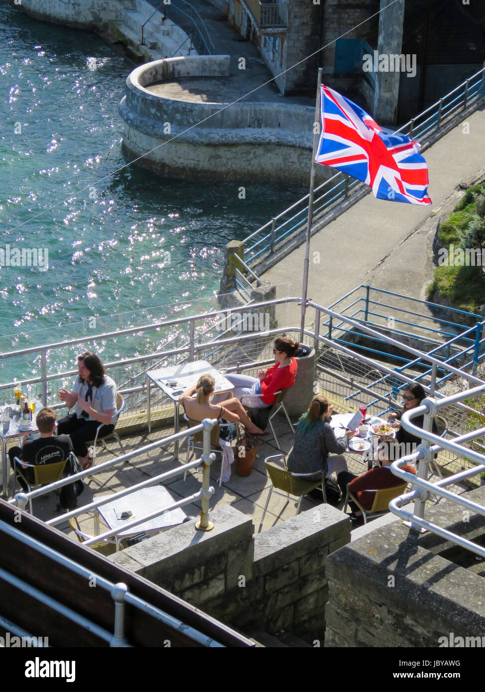 Les gens assis en terrasse de café sur Plymouth Hoe prendre des rafraîchissements aux beaux jours d'été à côté de la piscine. Tinside Soleil de scintillement de l'eau de mer bleu clair Banque D'Images