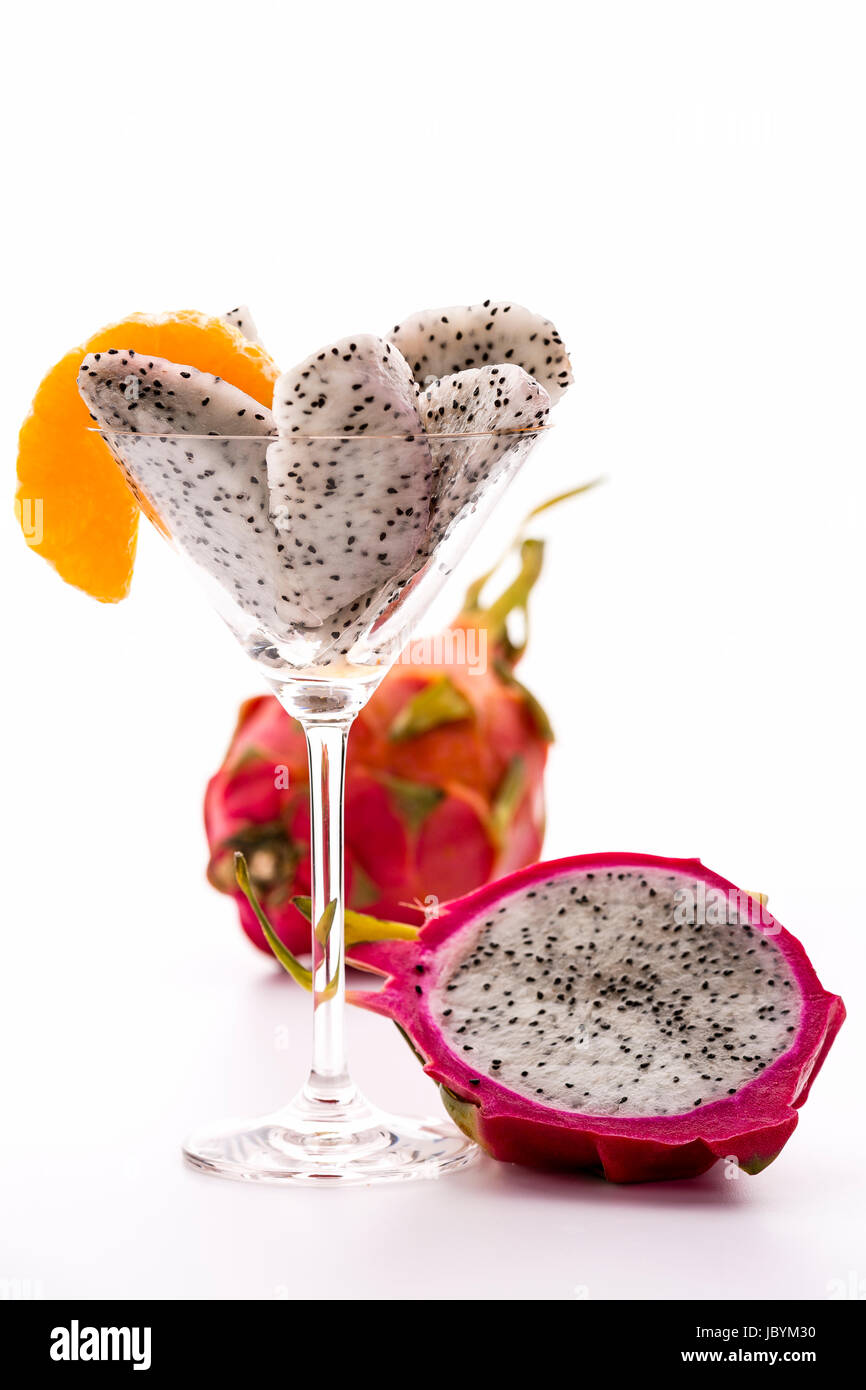 Des morceaux de pâte de pitaya assorted dans un verre à cocktail et décoré d'une tranche de mandarine. À côté il s'agit d'une moitié et, derrière elle, un fruit entier. Banque D'Images