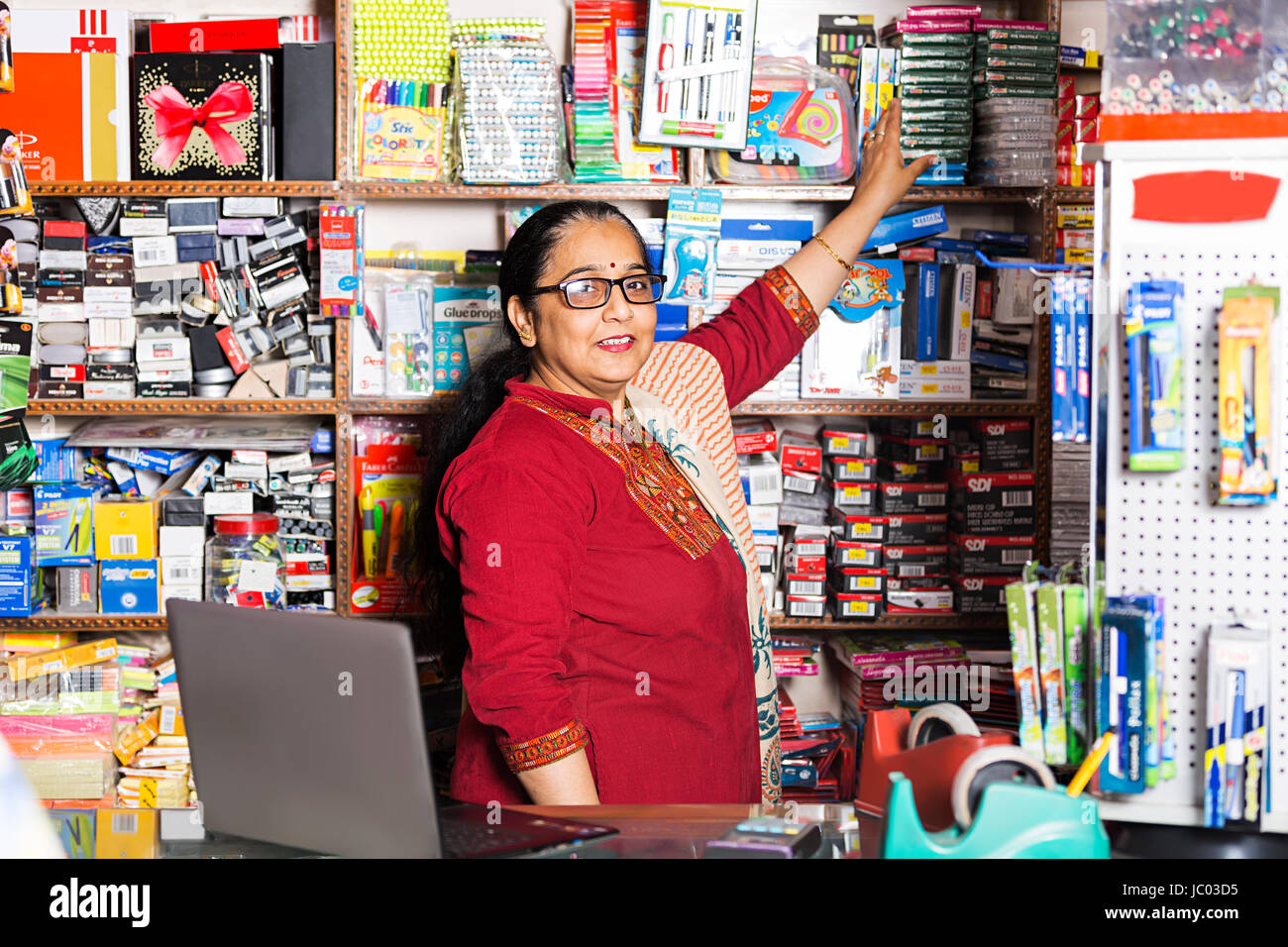 1 Indian shop keeper femme organiser produit sur rack dans l'arrêt shop Banque D'Images