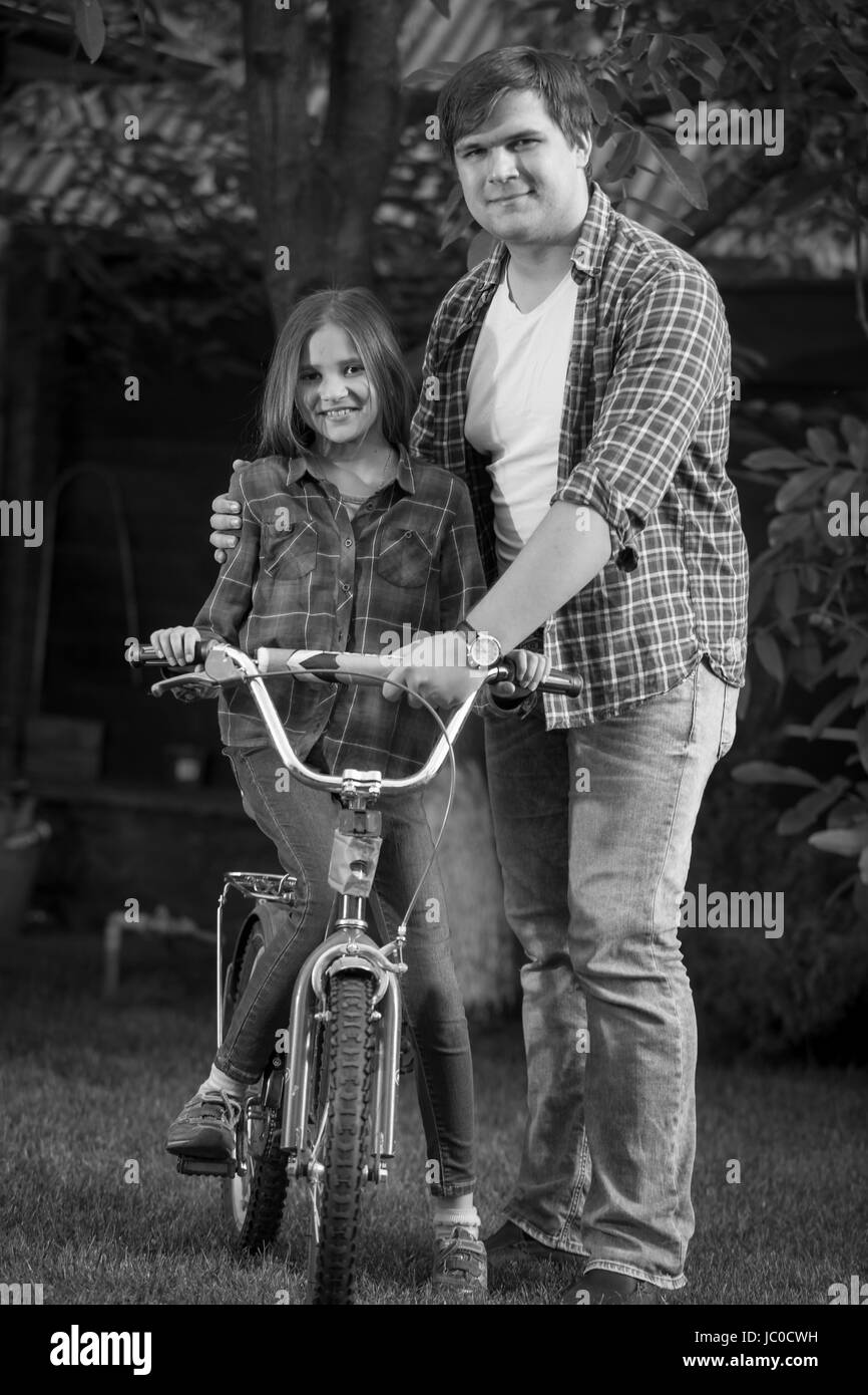 Portrait noir et blanc de l'heureux père d'enseigner son fille comment monter à vélo Banque D'Images