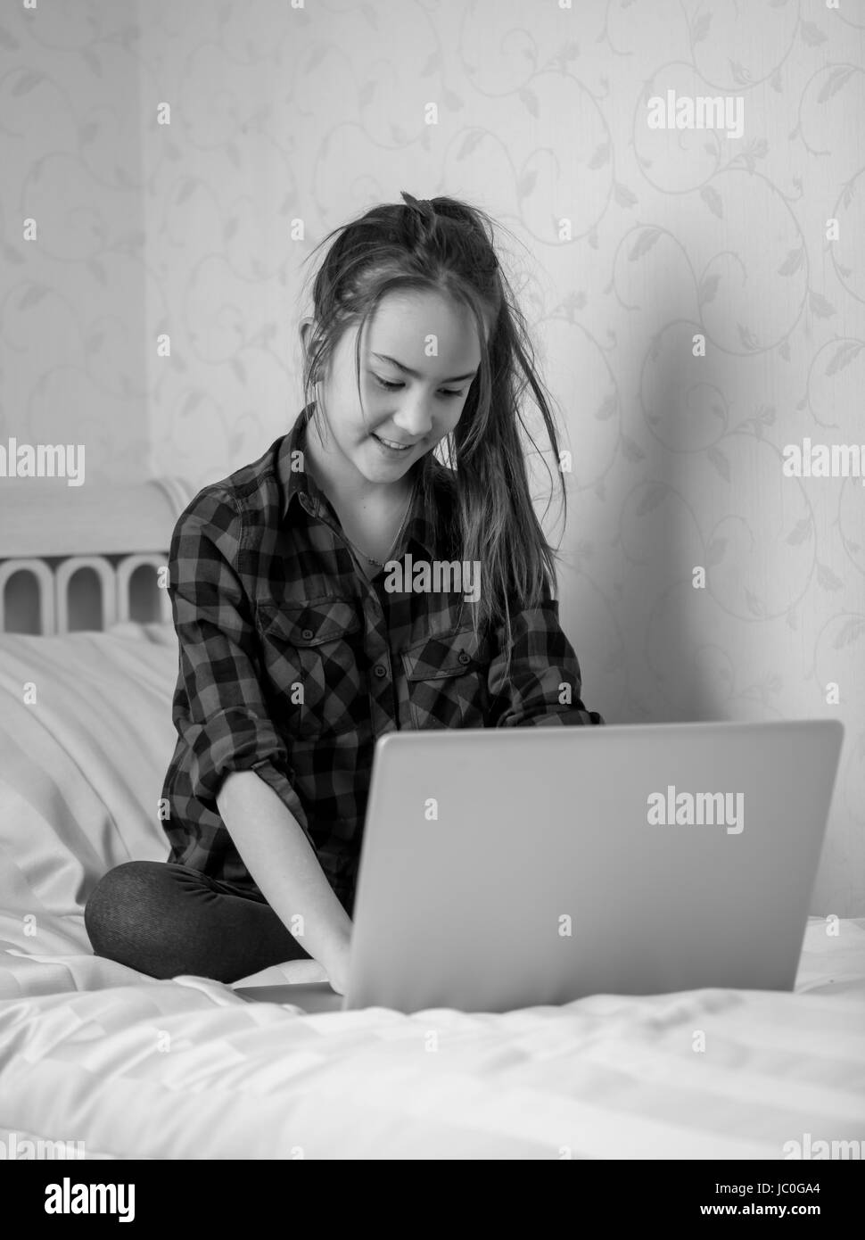 Photo en noir et blanc de teenage girl sitting on bed and using laptop Banque D'Images