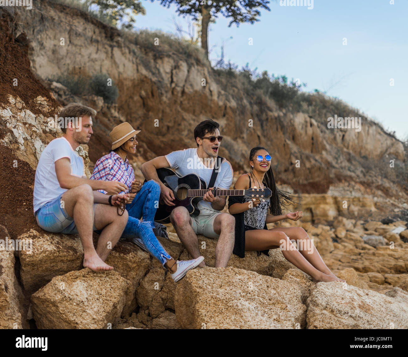 Amis assis sur des pierres sur la plage. l'homme est de jouer de la guitare. Banque D'Images