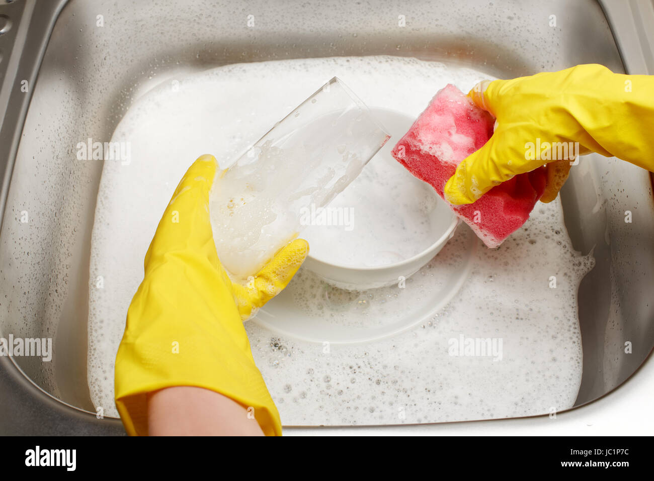 Close up de femmes dans les mains des gants en caoutchouc de protection jaune lave-verre rose avec éponge de nettoyage contre l'évier de cuisine pleine de mousse et tab Banque D'Images