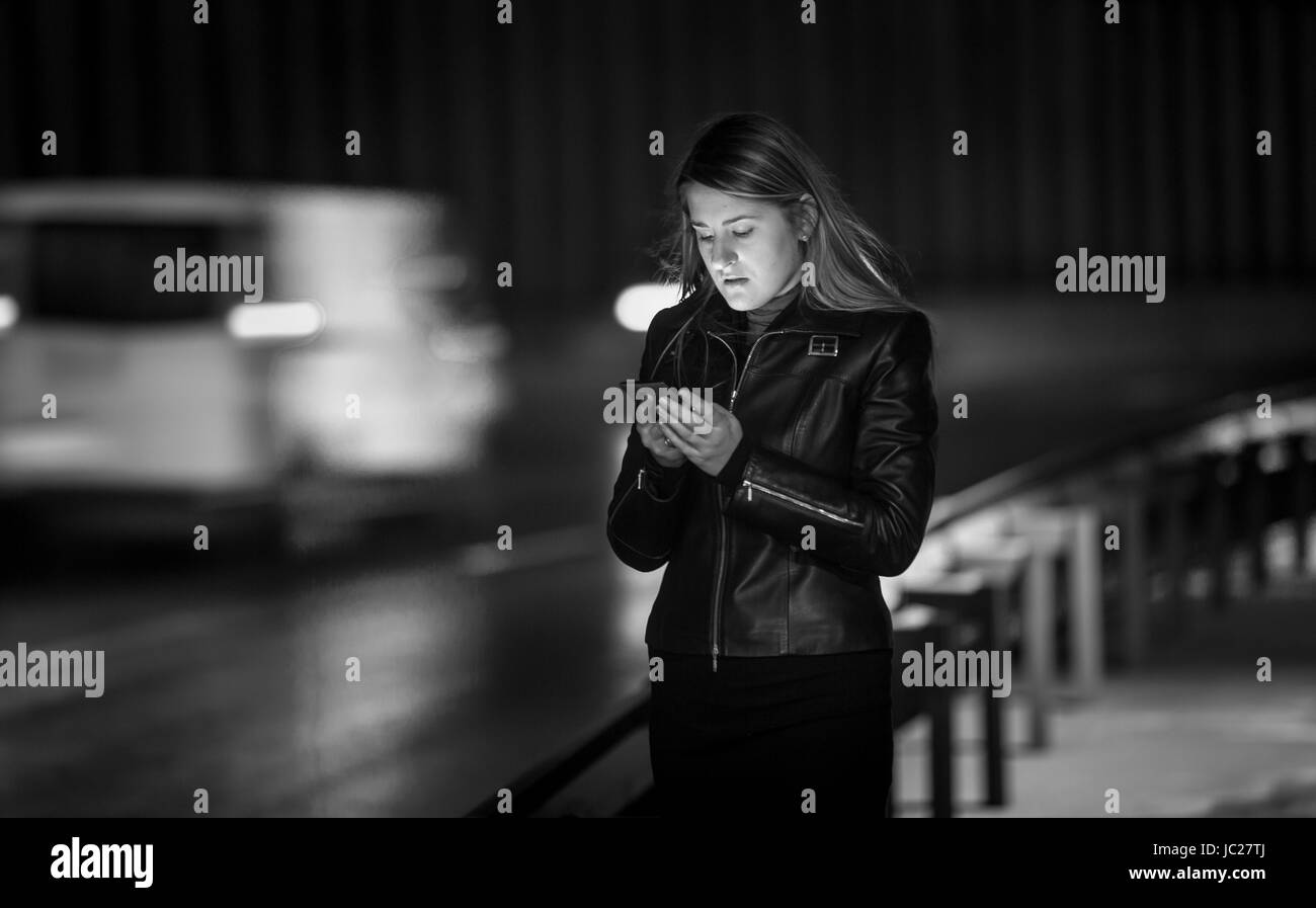 Le noir et blanc portrait of young woman typing message sur street at night Banque D'Images