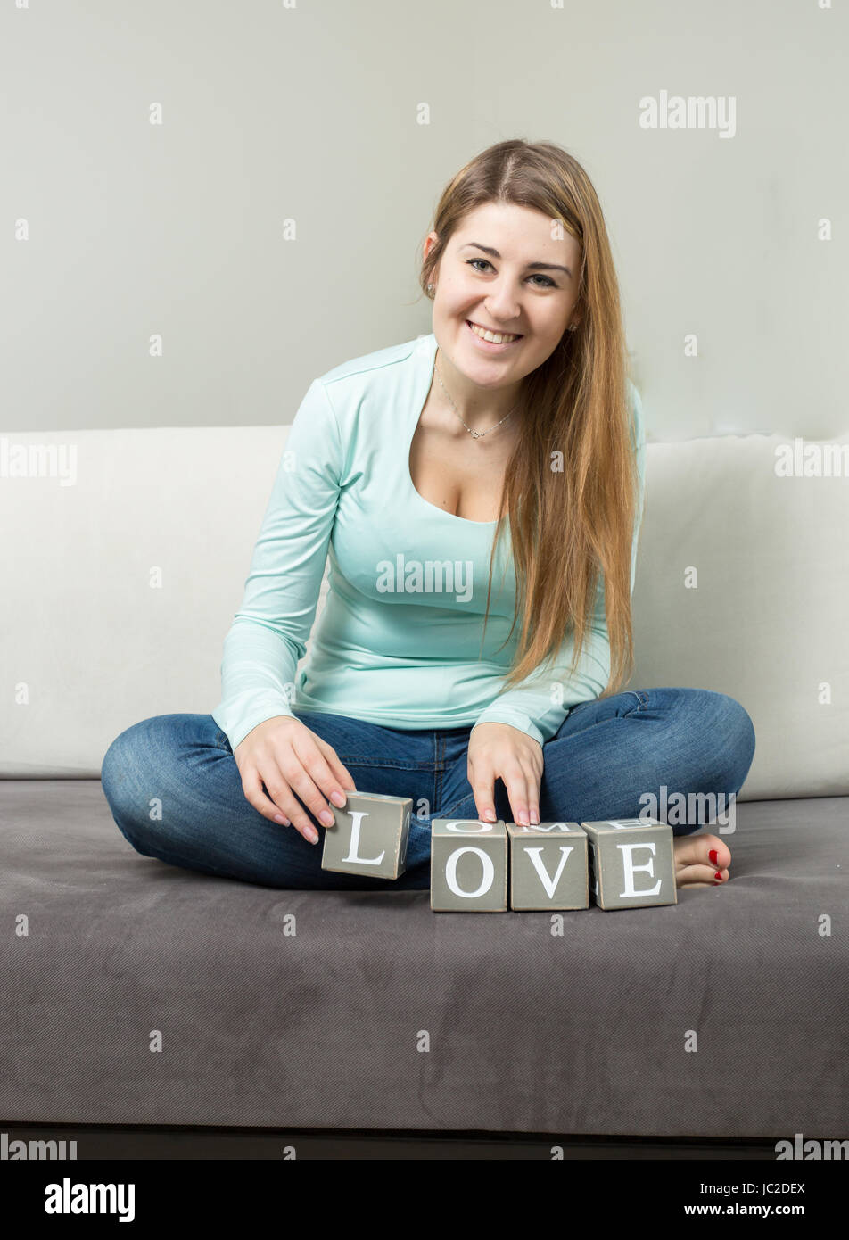 Jolie jeune femme rendant le mot 'Amour' de briques sur canapé Banque D'Images