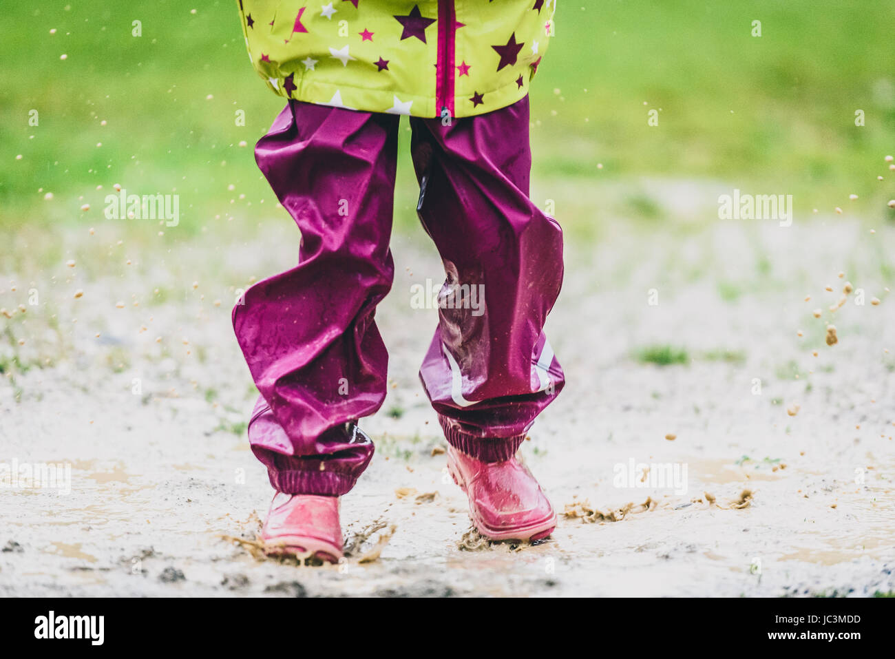 Les enfants dans des bottes en caoutchouc et des vêtements de pluie en saut  flaque. L'eau est d'éclabousser les pieds des filles comme elle est en  train de sauter et de jouer