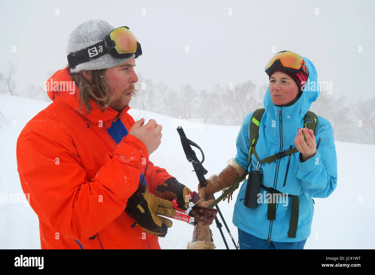 Une femme d'un skieur masculin de prendre une pause gourmande tout en ski de randonnée dans l'arrière-pays de Kiroro Skiing sur l'île du nord du Japon Hokkaido, célèbre pour l'extrême neige tomber. Ils ont heureusement manger du chocolat. Banque D'Images