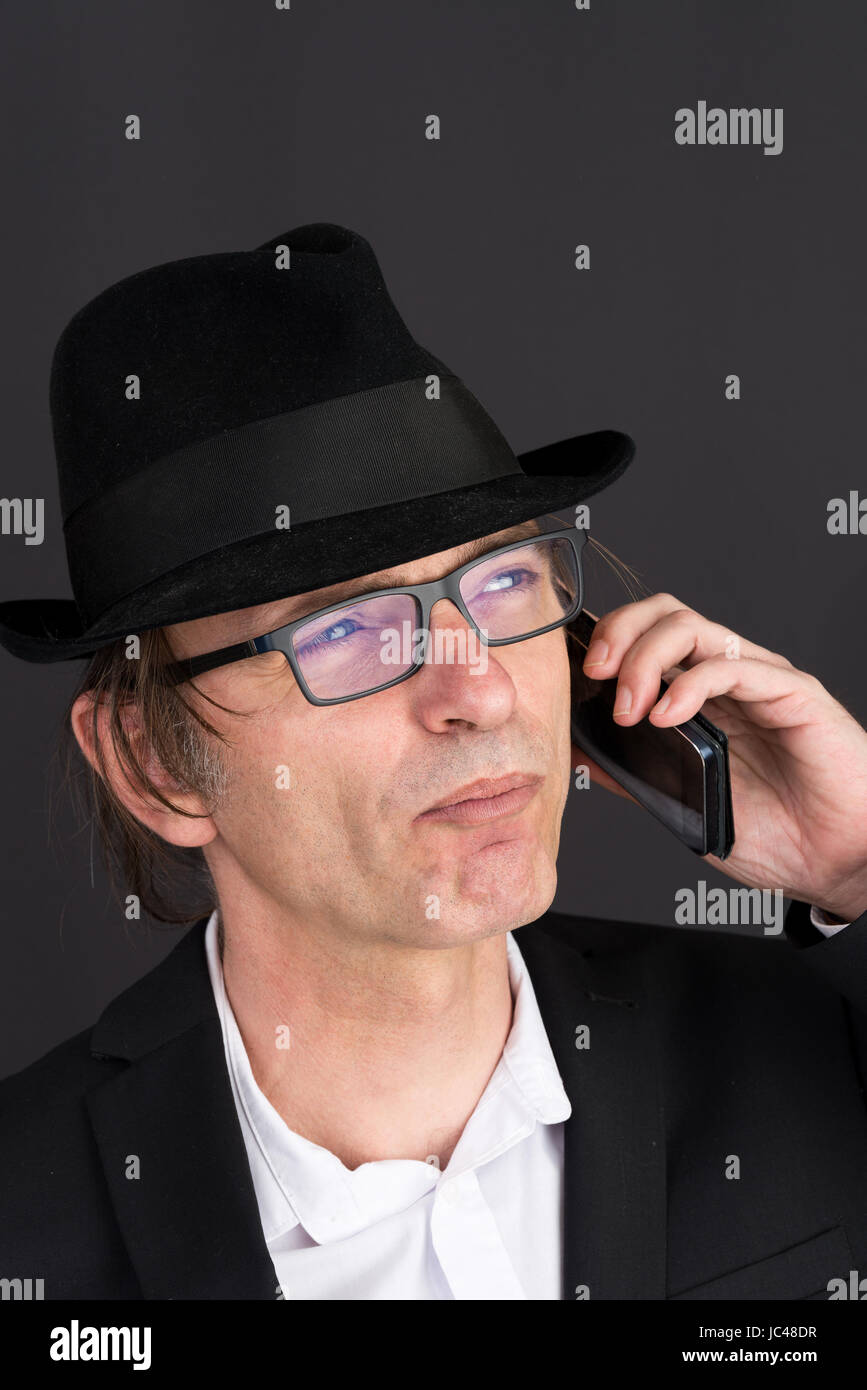 Portrait d'un homme d'âge moyen en tailleur et hat effectuer un appel téléphonique - studio shot sur fond sombre Banque D'Images