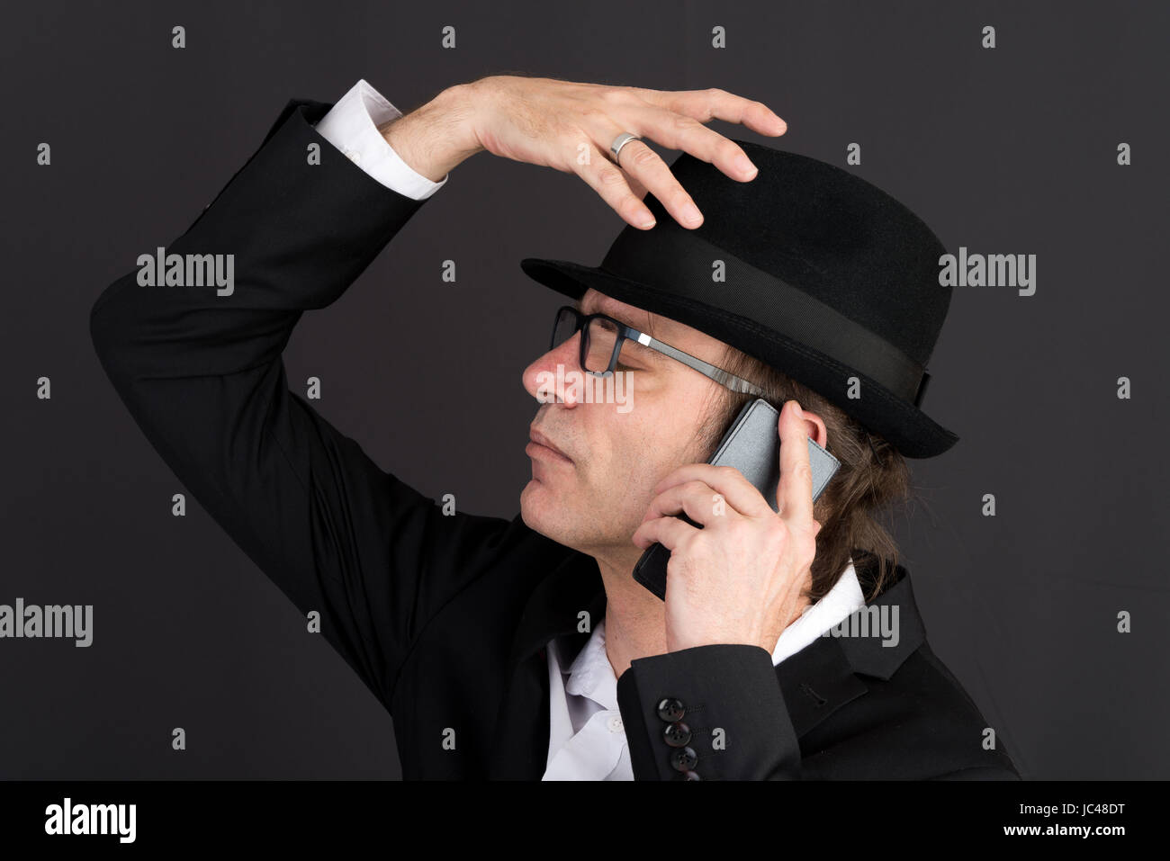 Portrait d'un homme d'âge moyen en tailleur et hat effectuer un appel téléphonique - studio shot sur fond sombre Banque D'Images
