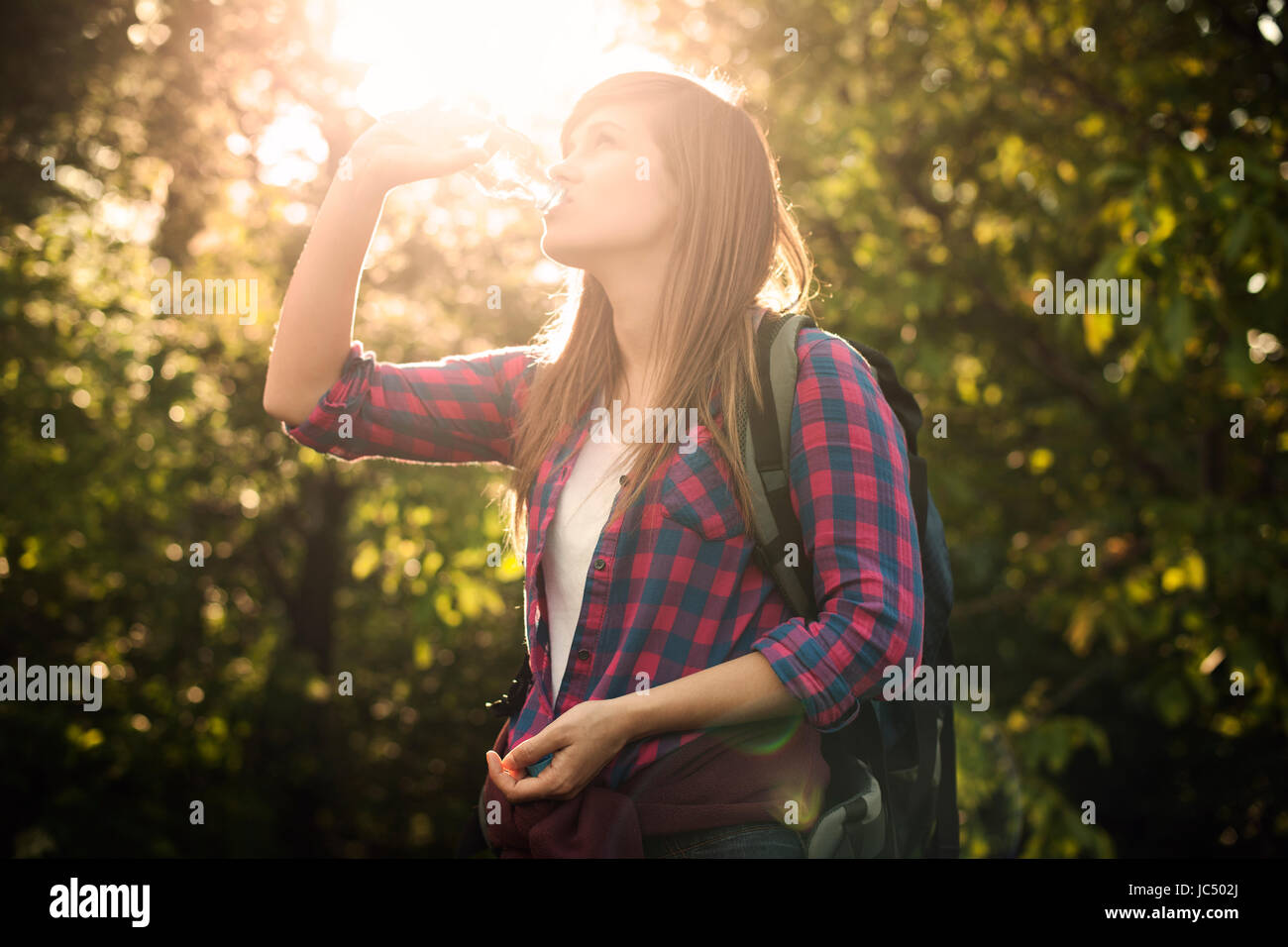 Belle female hiker l'eau potable en forêt au coucher du soleil Banque D'Images