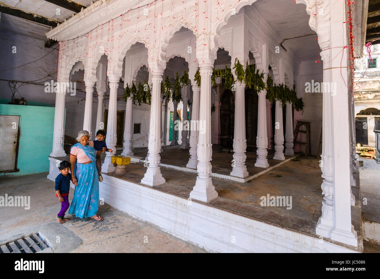 Une femme avec deux petits enfants est passé à pied d'un petit temple hindou de piliers blancs dans la banlieue godowlia Banque D'Images