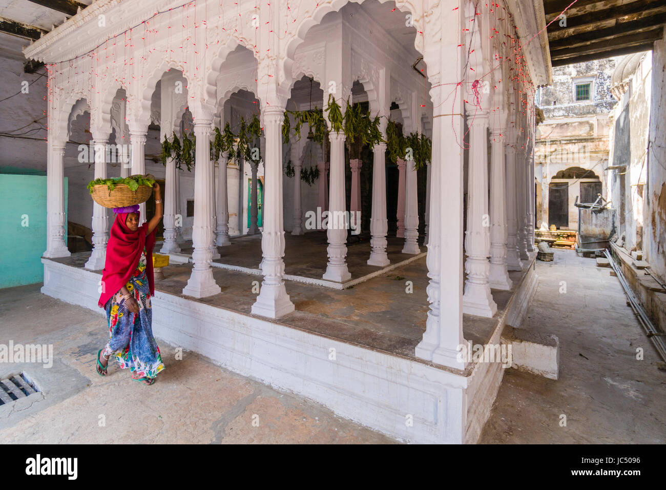 Une femme, portant un panier sur sa tête, est passé à un petit temple hindou de piliers blancs dans la banlieue godowlia Banque D'Images