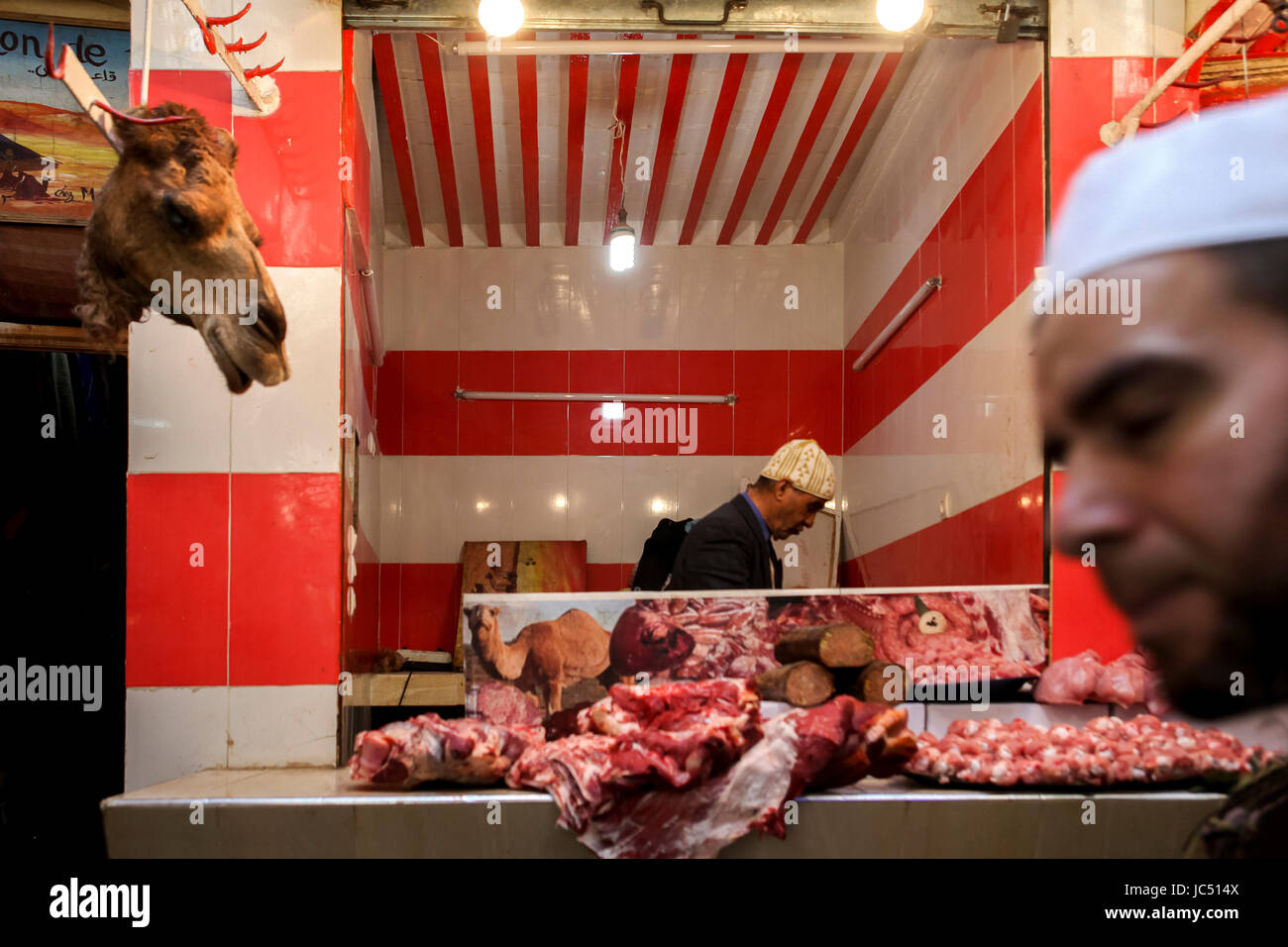 Un homme passe devant une tête de chameau accroché à l'extérieur d'un stand de boucherie à Fès, au Maroc. Banque D'Images