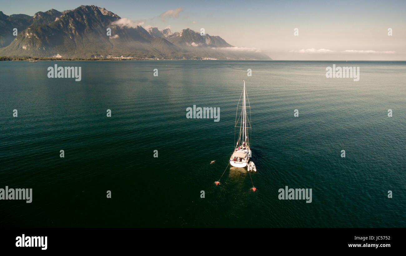 Bateau à voile ancré dans le lac de Genève dans le Canton de Vaud sur une belle journée avec des montagnes en arrière-plan et de ciel bleu. Banque D'Images