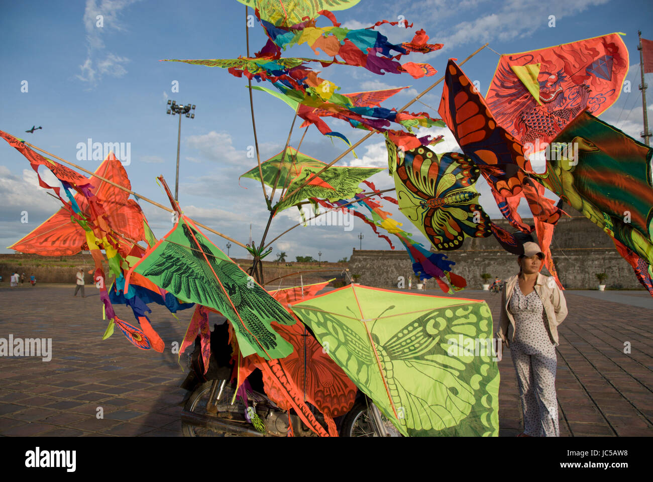 Une femme se distingue par un vélo orné de cerfs-volants colorés, ci-dessous le drapeau de la tour de l'enceinte de la Citadelle impériale, un site à douves dans l'ancien, partie historique de la ville de Hue, maintenant un site du patrimoine mondial de l'UNESCO pour son architecture et son importance historique. Hue a longtemps été politiquement et culturellement au cœur du Vietnam, et est maintenant un arrêt touristique populaire. Banque D'Images