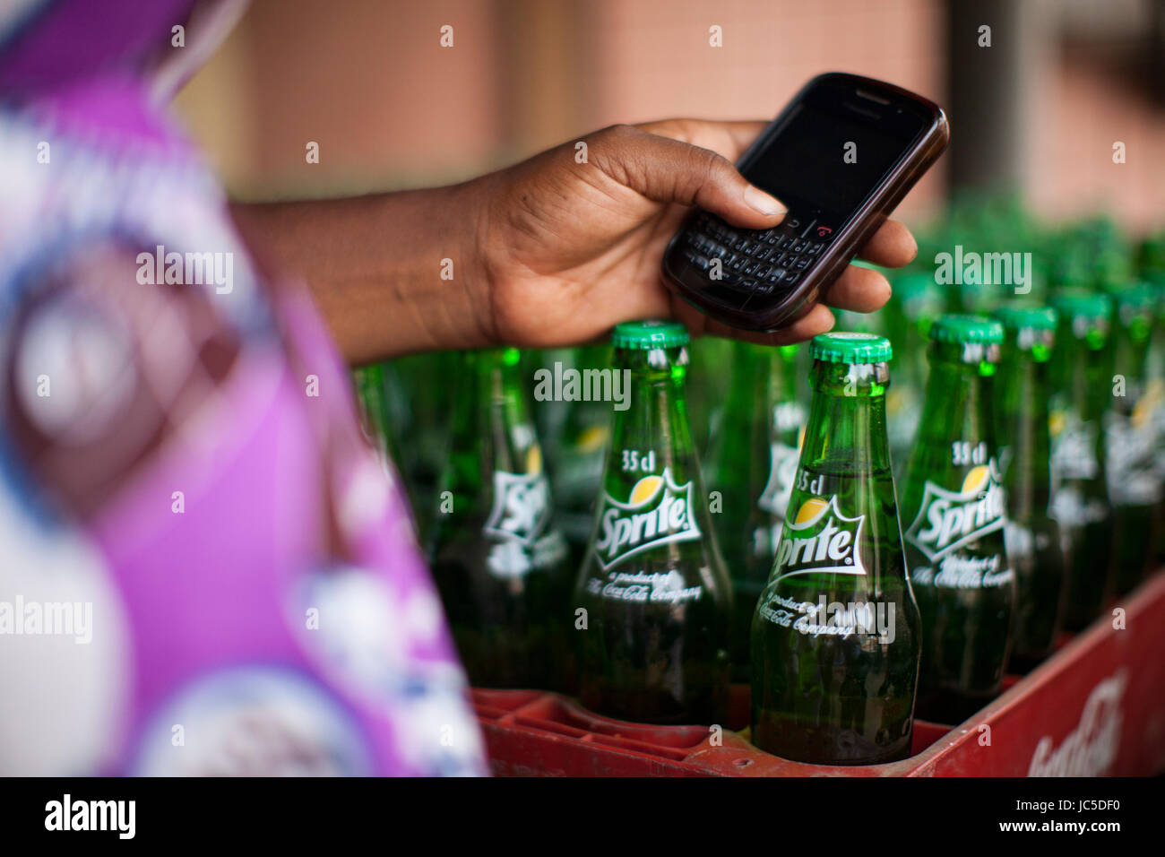 Une femme d'affaires utilisant son téléphone portable avec des bouteilles de limonade dans une caisse à côté d'elle, Nigeria, Afrique Banque D'Images Une femme d'affaires utilisant son téléphone portable avec des bouteilles de limonade dans une caisse à côté d'elle, Nigeria, Afrique Banque D'Images